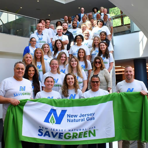 SAVEGREEN team members hold SAVEGREEN banner indoors, representing community and energy-efficiency commitment.