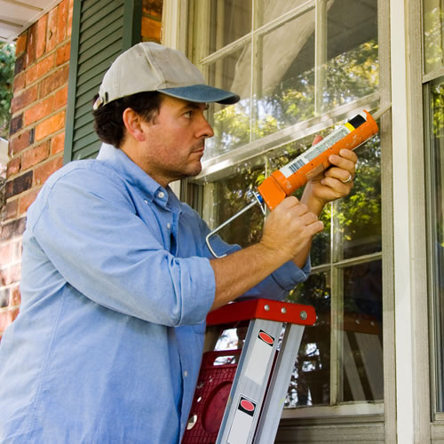Person seals window frame with caulk, showing more affordable energy-saving upgrades for income-qualified households.