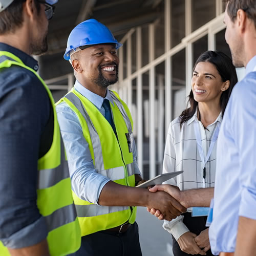 Contractor and business professionals shake hands on-site, showing collaboration on energy-efficient upgrades.