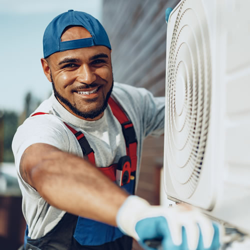 Technician in blue cap installs AC unit, representing hands-on training and careers in energy efficiency.